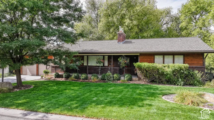 Brick and horizontal wood siding exterior with a covered porch, front lawn, and mature trees