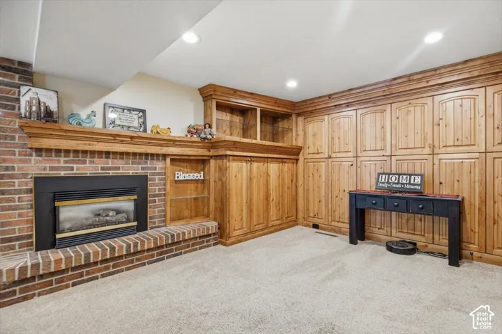 Brick fireplace with a wood-finish mantel and hearth, built-in shelving, extensive wood-finish cabinetry, recessed lighting, and carpet flooring