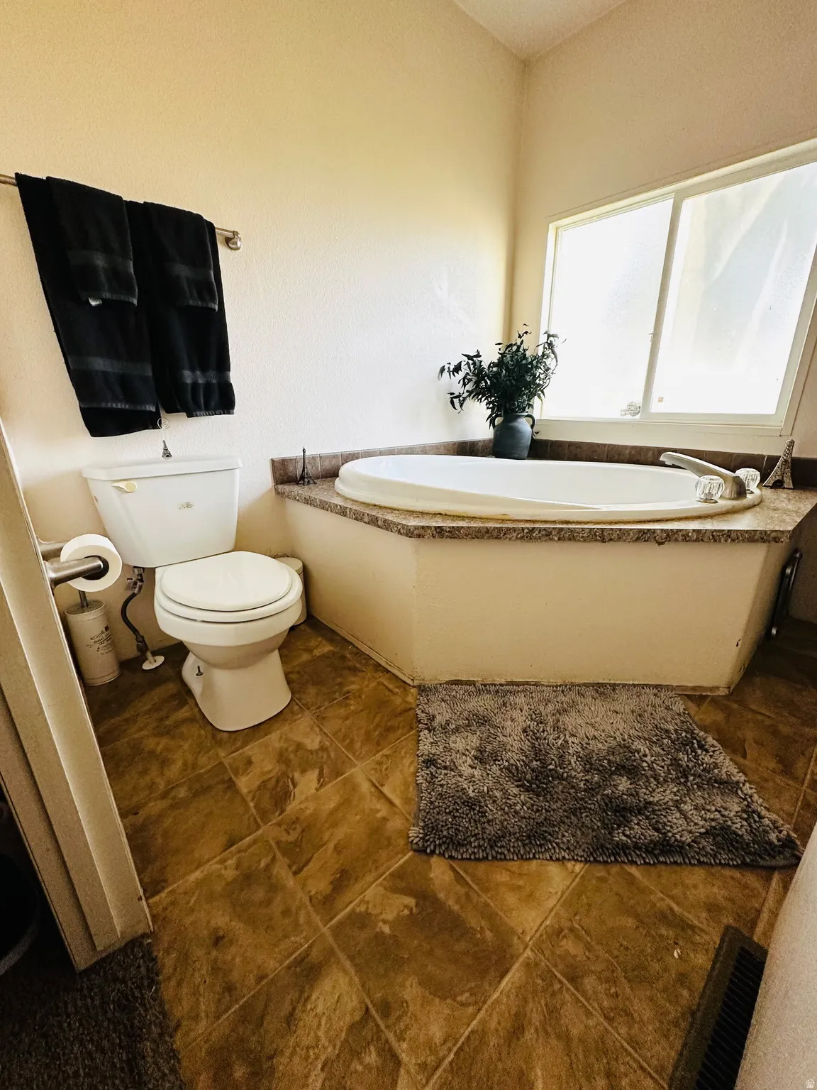 Built-in soaking tub with a stone-finish surround, large window, and tile flooring