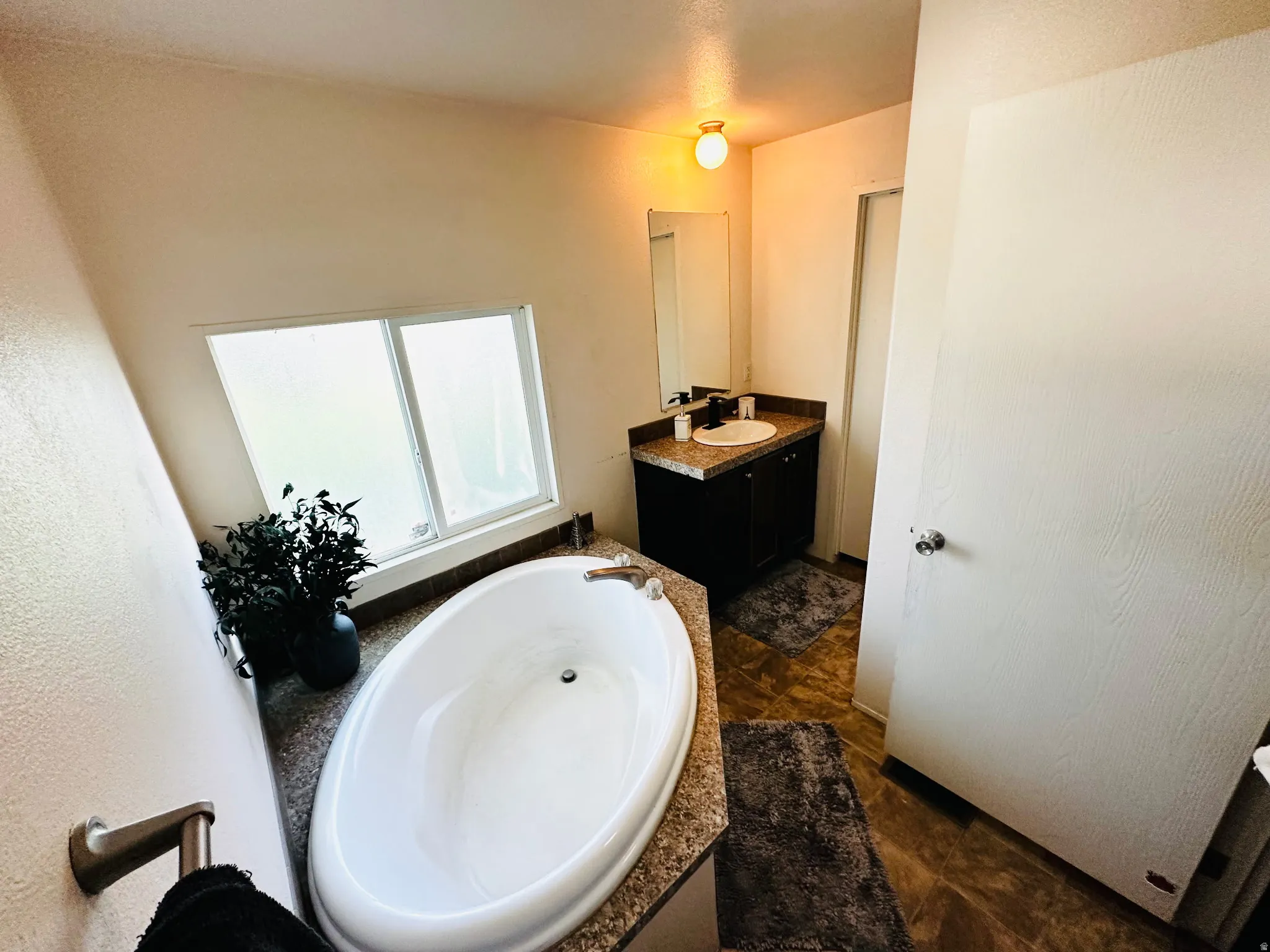 Freestanding oval bathtub, single vanity with integrated sink, dark wood-finish cabinetry, and a large privacy window