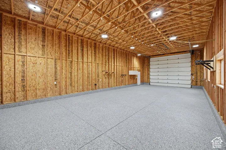 Spacious unfinished interior featuring exposed wooden framing, a segmented overhead door, and a speckled gray epoxy floor