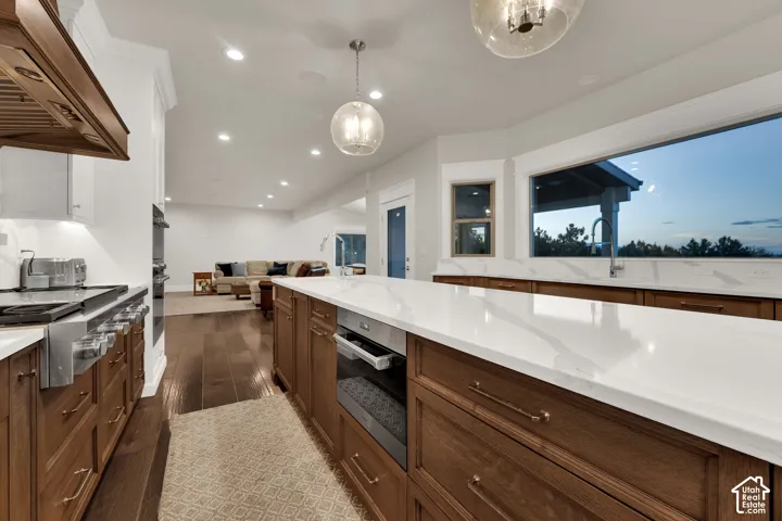 Gourmet kitchen featuring a large central island with a built-in oven, white countertops, rich wood cabinetry, and a stainless steel gas range with a matching range hood