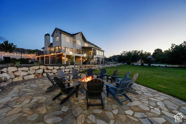 Stone patio with a built-in fire pit, expansive lawn, and tiered landscaping featuring natural stone retaining walls