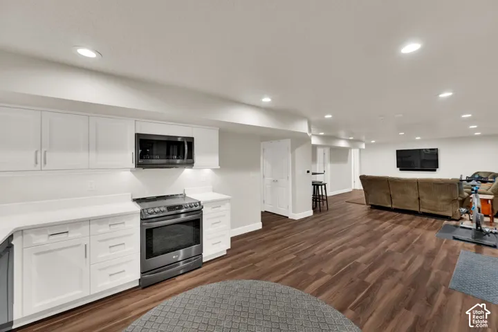 White shaker-style cabinetry with integrated microwave and range, light-toned countertops, wood-finish flooring, and recessed lighting