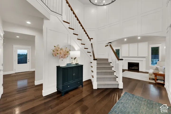 Two-story entry featuring dark wood-finish flooring, a grand staircase with carpeted treads and white risers, and extensive wainscoting