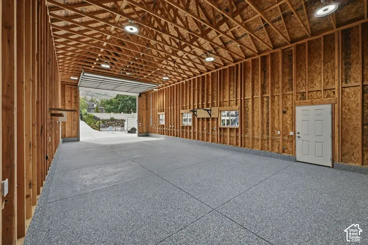 Expansive open space featuring an exposed wood-frame ceiling, textured gray flooring, multiple recessed light fixtures, and a white panel door