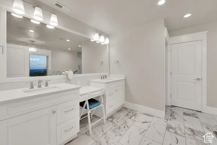 Primary bathroom.  Dual vanities with undermount sinks, expansive wall-mounted mirror, vanity lighting fixtures, integrated dressing table, and marble-look tile flooring