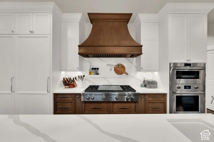 White perimeter cabinetry, a wood-finish range hood, stainless steel appliances, a Wolf appliance, and a light-toned countertop