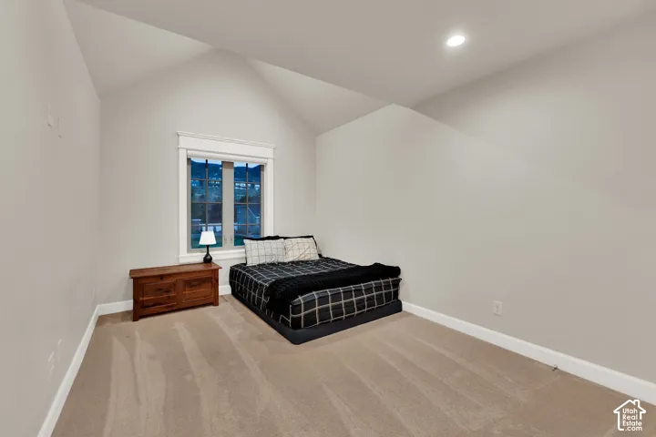 Vaulted ceiling, recessed lighting, neutral tone carpeting, white window trim, and a double-paned window