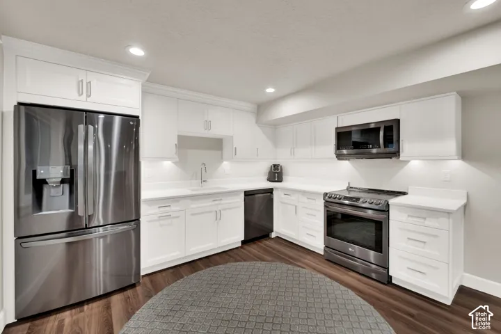 White shaker-style cabinetry with matte silver hardware, stainless steel appliances, solid surface countertops, recessed lighting, and wood-finish flooring