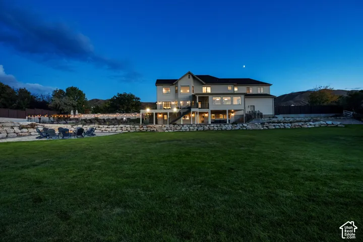 Expansive rear lawn, multi-level patio with stone retaining walls, and a lower-level covered patio