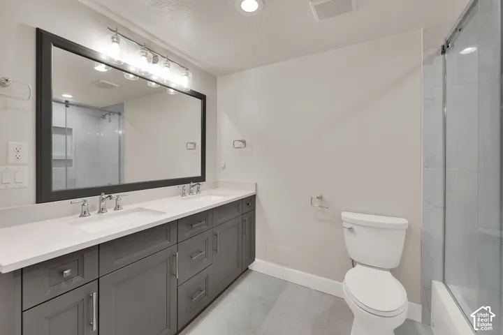 Dual vanity with undermount sinks and chrome fixtures, framed mirror with vanity lighting, glass-enclosed shower, and tile flooring