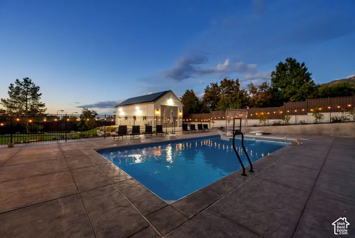 Expansive stamped concrete pool deck featuring an in-ground swimming pool, a dedicated pool house with solar panels, and a black wrought iron perimeter fence