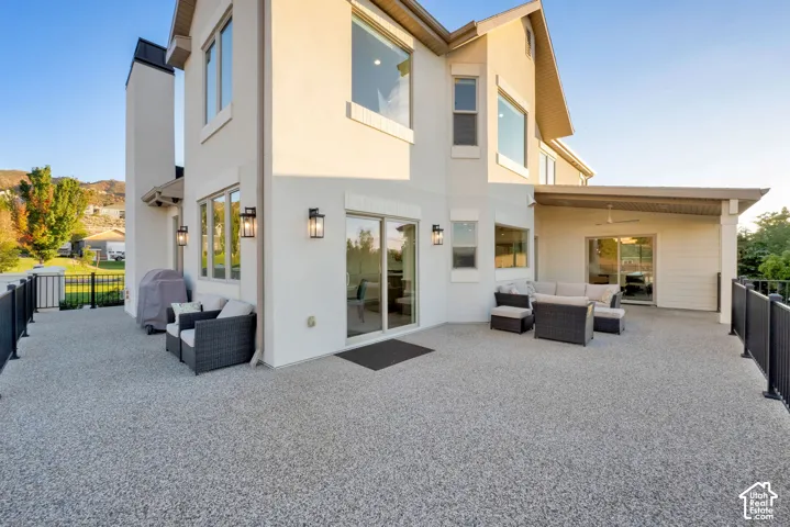 Expansive speckled patio featuring a covered area with a ceiling fan, multiple sliding glass doors, and black metal railings