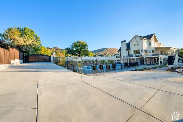 Expansive concrete patio with a fenced in-ground pool, elevated deck, and a multi-story exterior