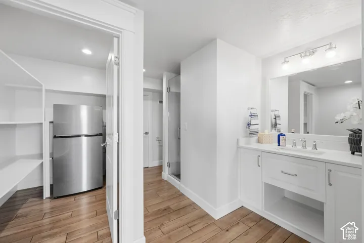 Pool bathroom.  White vanity with integrated sink, wood-finish flooring, glass-enclosed shower, stainless steel refrigerator, and built-in shelving