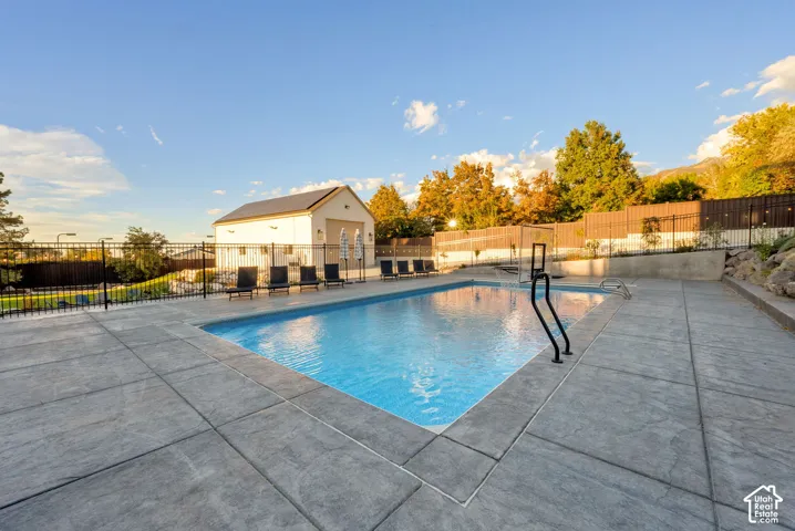 Expansive swimming pool with concrete decking, surrounded by a black metal fence