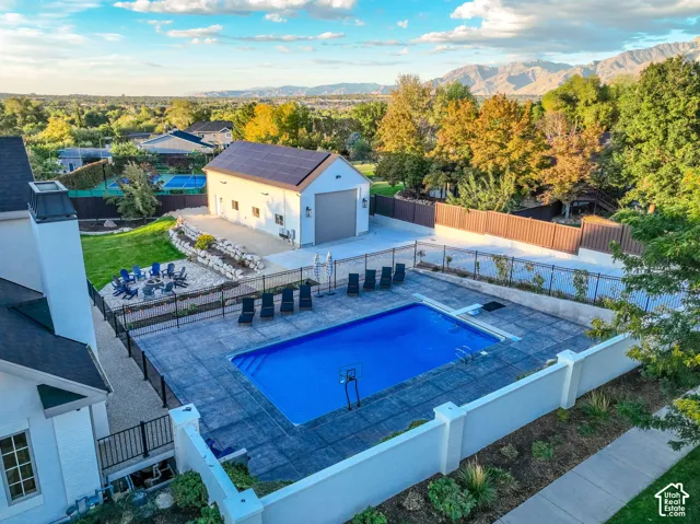 Outdoor pool with expansive paver surround, detached garage with solar panels, lush lawn, and stone retaining wall