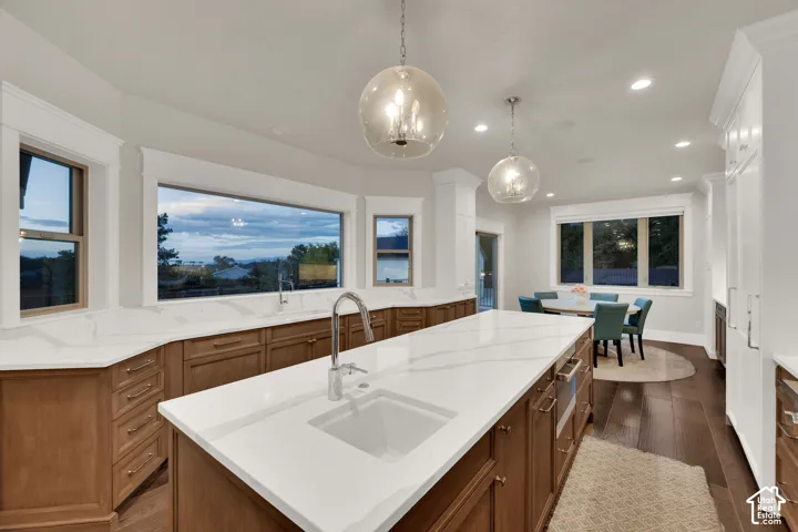 Expansive kitchen featuring a large island with an undermount sink, white countertops, wood-finish cabinetry, and recessed lighting