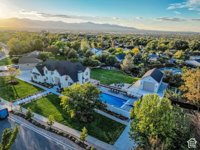White exterior with black roof, expansive green lawn, rectangular pool with surrounding patio, detached garage, and distant mountain backdrop