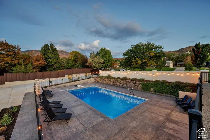 Rectangular in-ground swimming pool with stamped concrete surround, bordered by a solid privacy fence and retaining wall