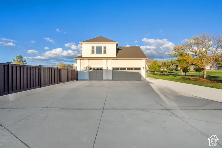 Two-story residence featuring a private fence, expansive concrete driveway, and two separate garage doors