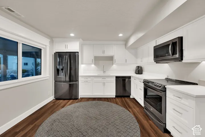 Modern kitchen featuring white cabinetry, dark wood-finish flooring, recessed lighting, and stainless-steel appliances