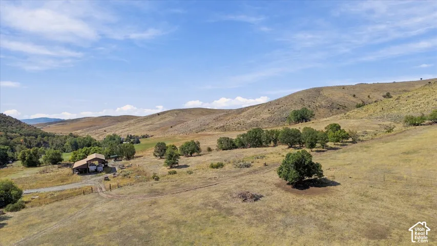 Expansive property featuring a residence, detached outbuilding, and mature trees amidst rolling hills