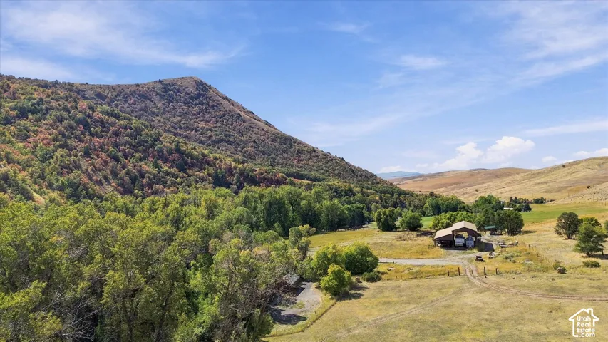 Expansive property featuring a residence, mature trees, a mountainous backdrop, and open fields