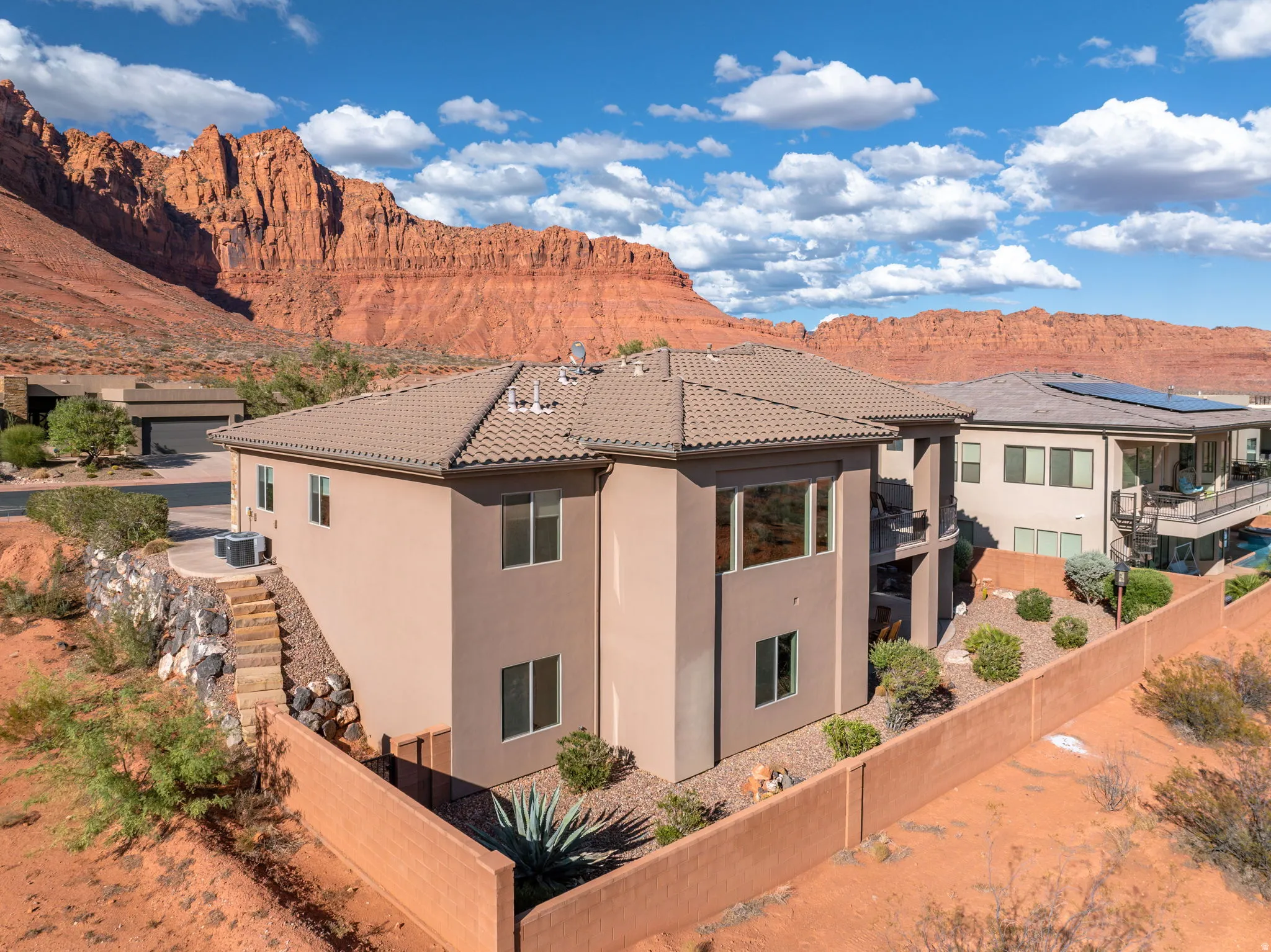 Stucco exterior residence with a tile roof, multiple windows, and a tiered rock retaining wall leading to a private outdoor space
