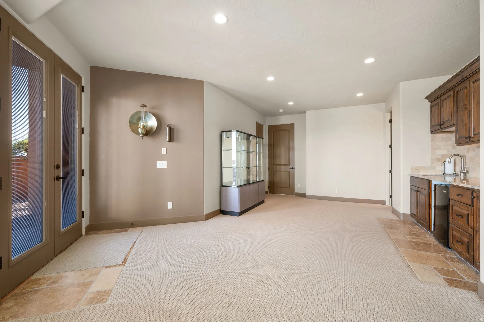 Full-light French doors, recessed ceiling lighting, a wet bar with under-counter refrigerator, tile flooring, and a display cabinet