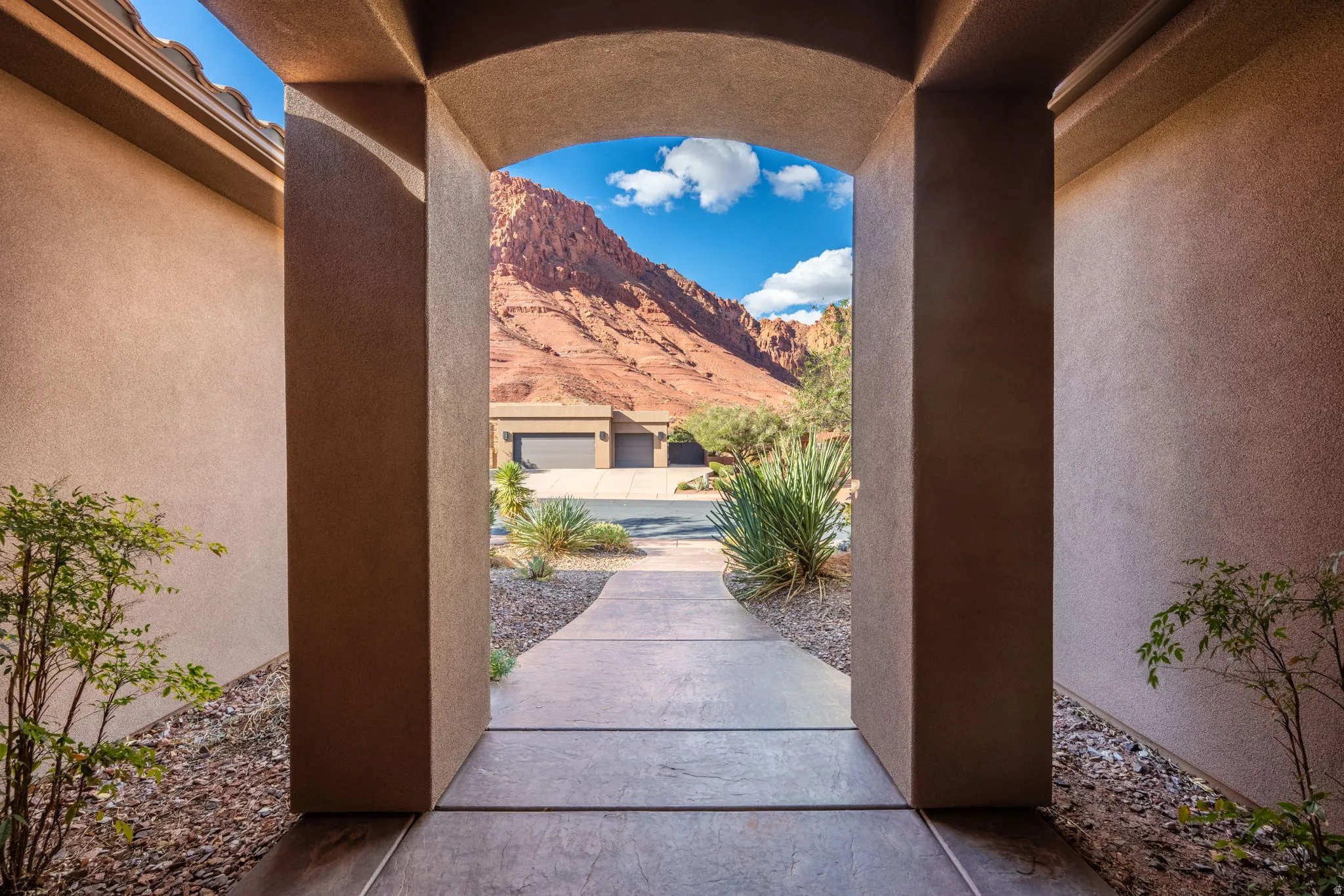 Archway entrance with a paved walkway, surrounded by low-maintenance landscaping and framed by a prominent mountain backdrop