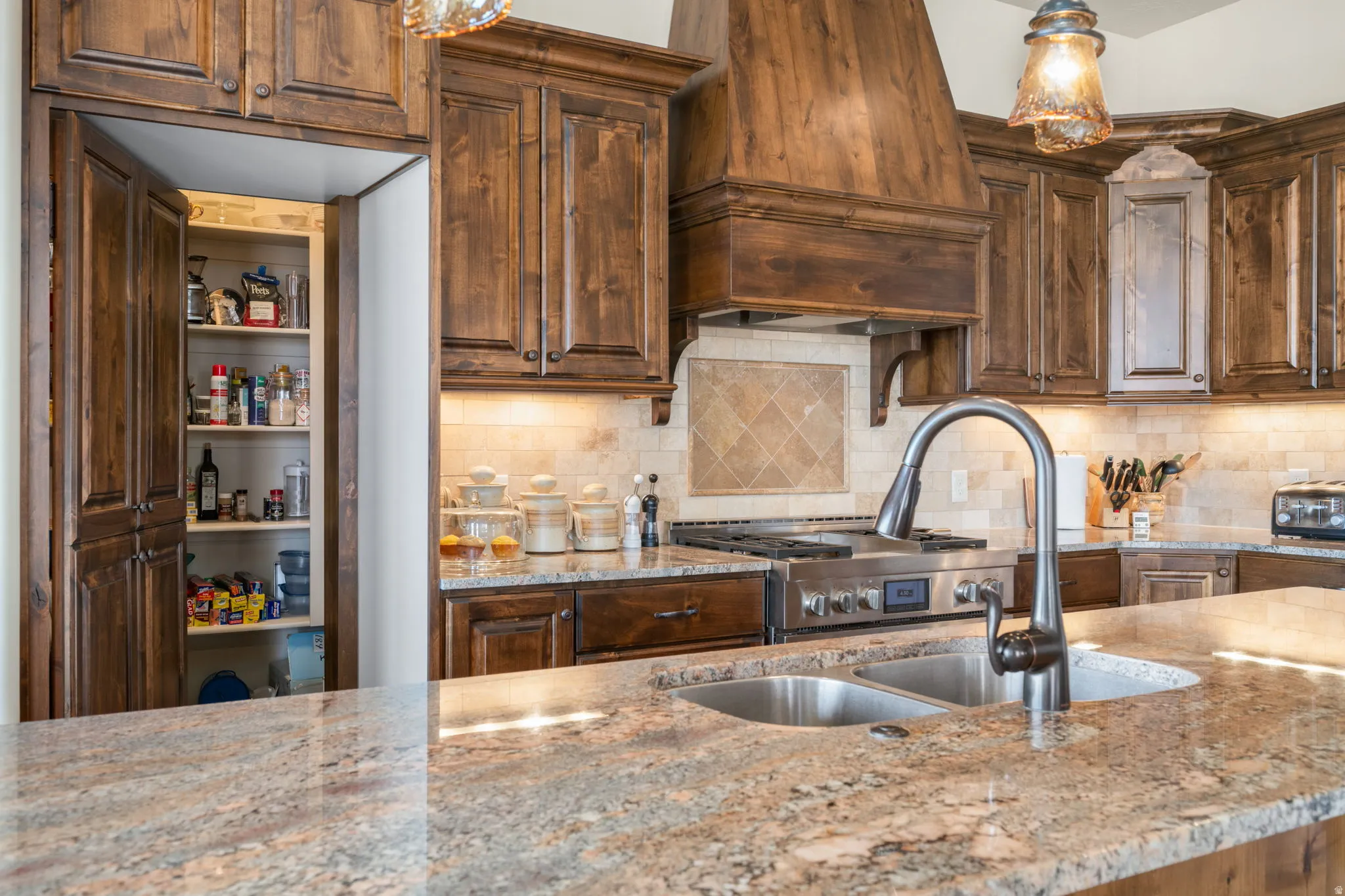Expansive granite countertops, stainless steel double basin sink with gooseneck faucet, professional-grade range, custom wood cabinetry, and a built-in pantry