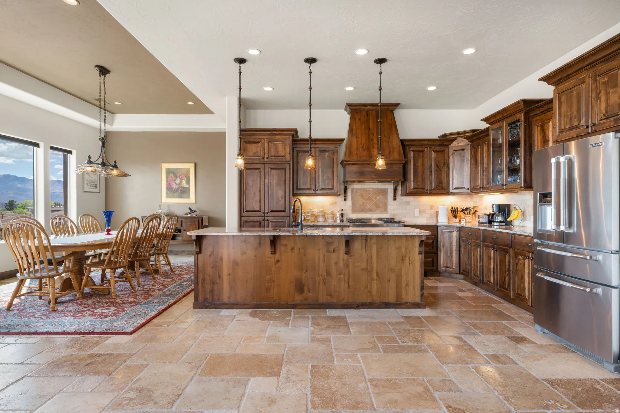 Gourmet kitchen featuring a large central island, stainless steel appliances, extensive wood cabinetry, and stone tile flooring