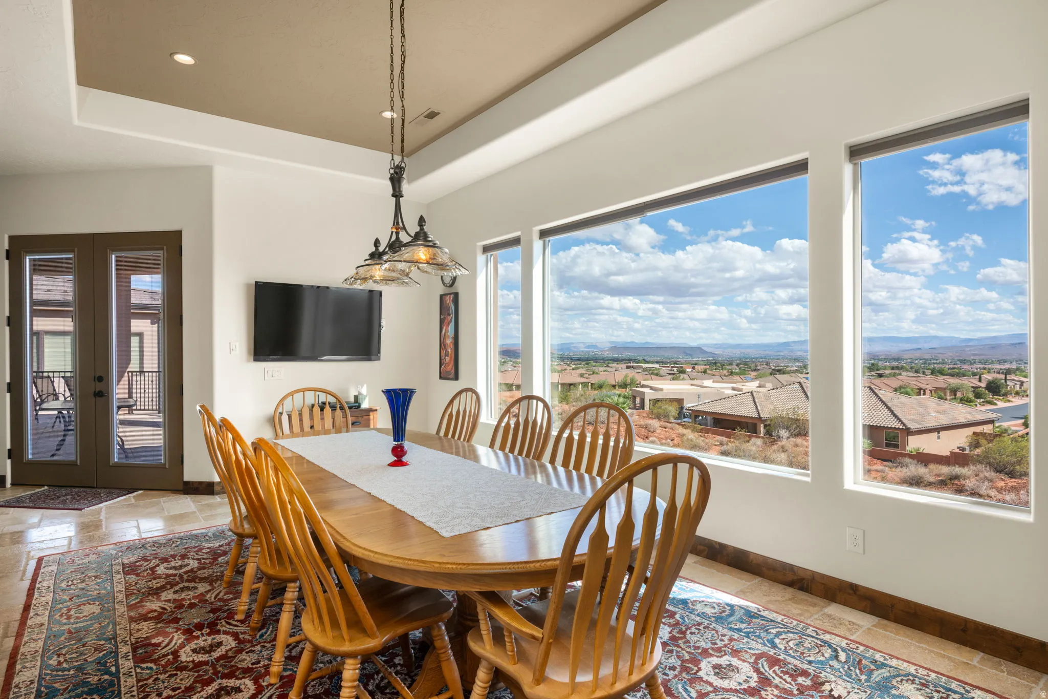 Recessed ceiling with integrated lighting, glass-paneled French doors, tile flooring, and multiple expansive windows showcasing the distant landscape