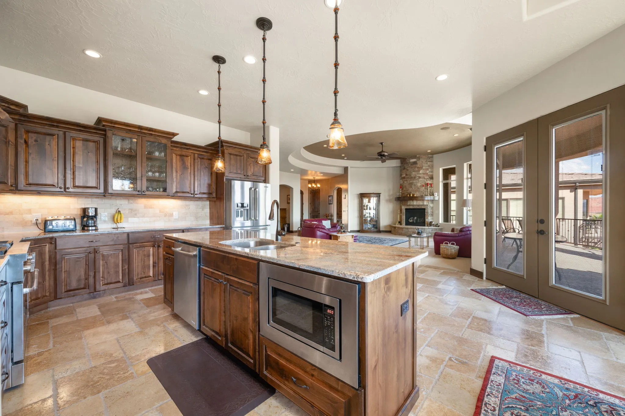 Gourmet kitchen featuring wood cabinetry, stainless steel appliances, a large island with a built-in microwave, and stone tile flooring