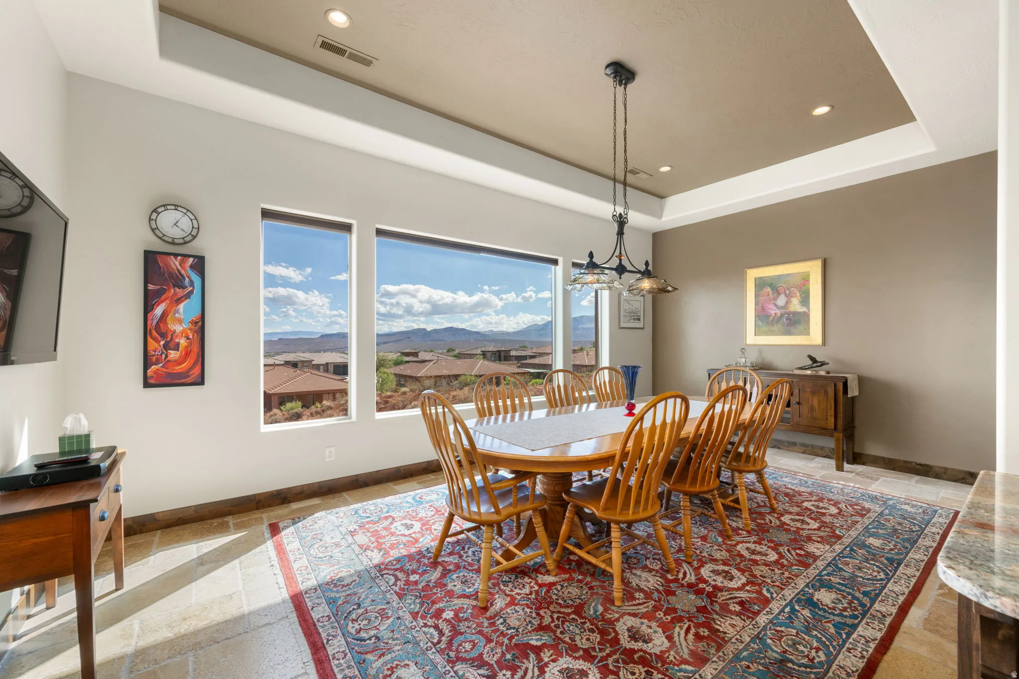 Large windows with distant scenery, tray ceiling with recessed lighting, stone tile flooring, and a decorative pendant light fixture