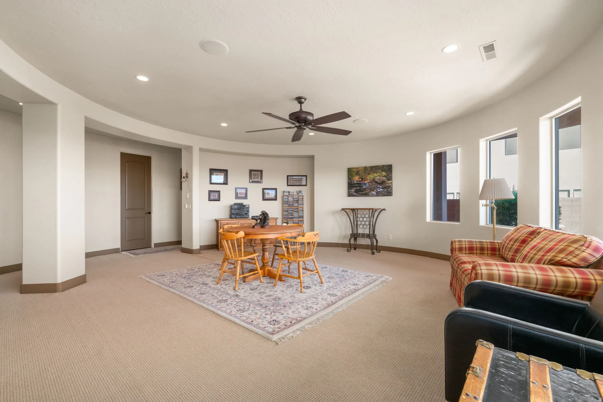 Curved architectural wall, recessed ceiling lighting, ceiling fan, multiple windows, and carpet flooring