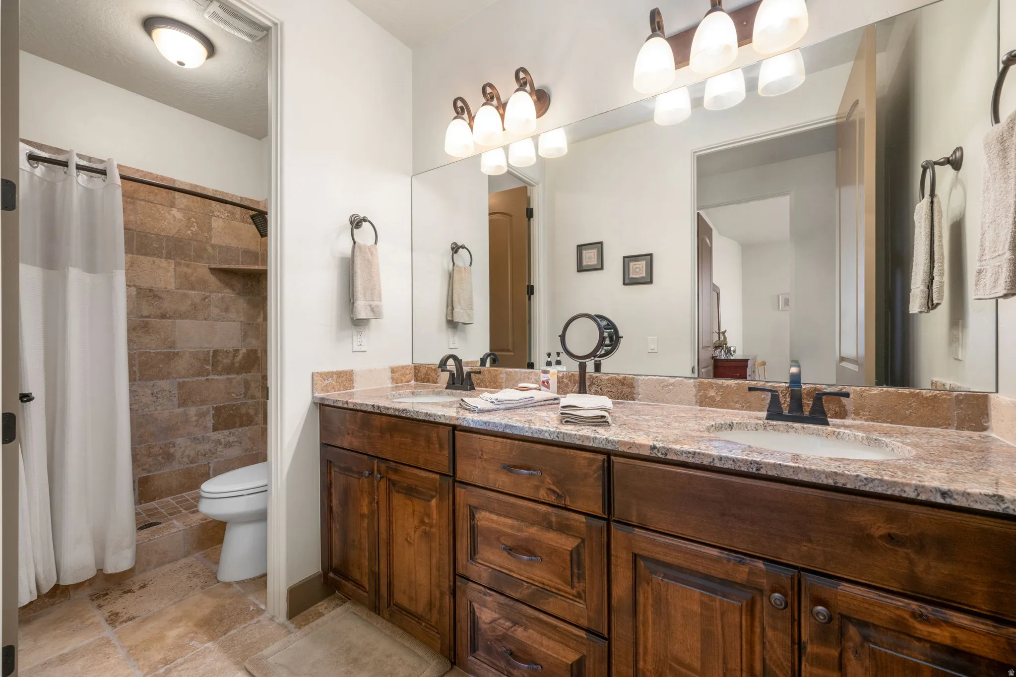 Dual vanity with integrated sinks, granite countertop, rich wood-finish cabinetry, and framed mirror