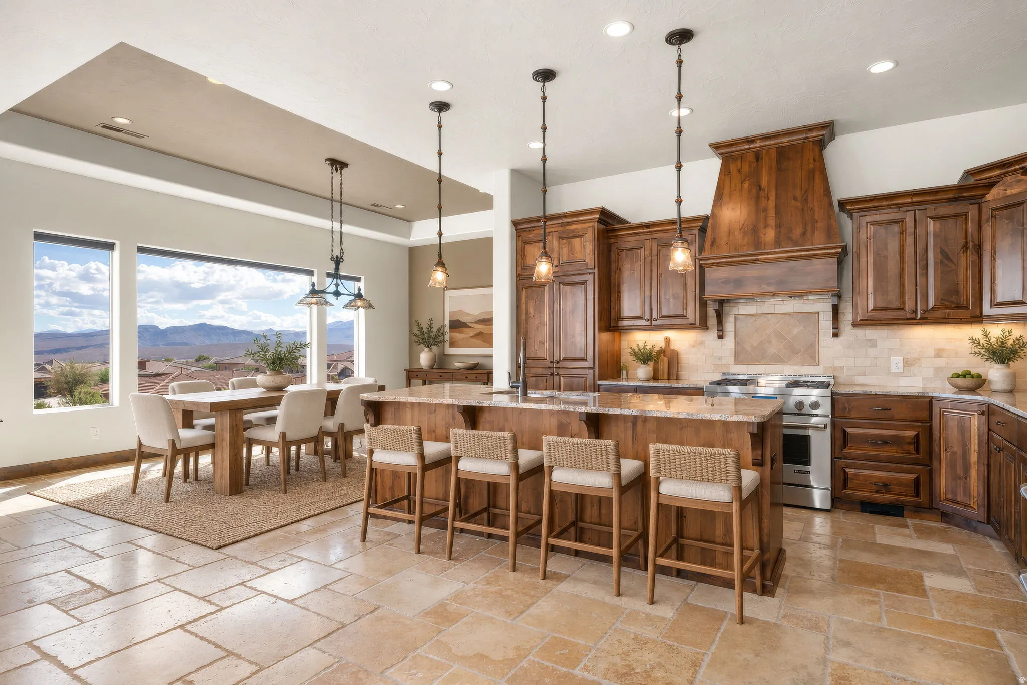 Expansive kitchen and dining area featuring stone tile flooring, a large kitchen island with counter seating, wood cabinetry, stainless steel appliances, and a dining area with multiple windows