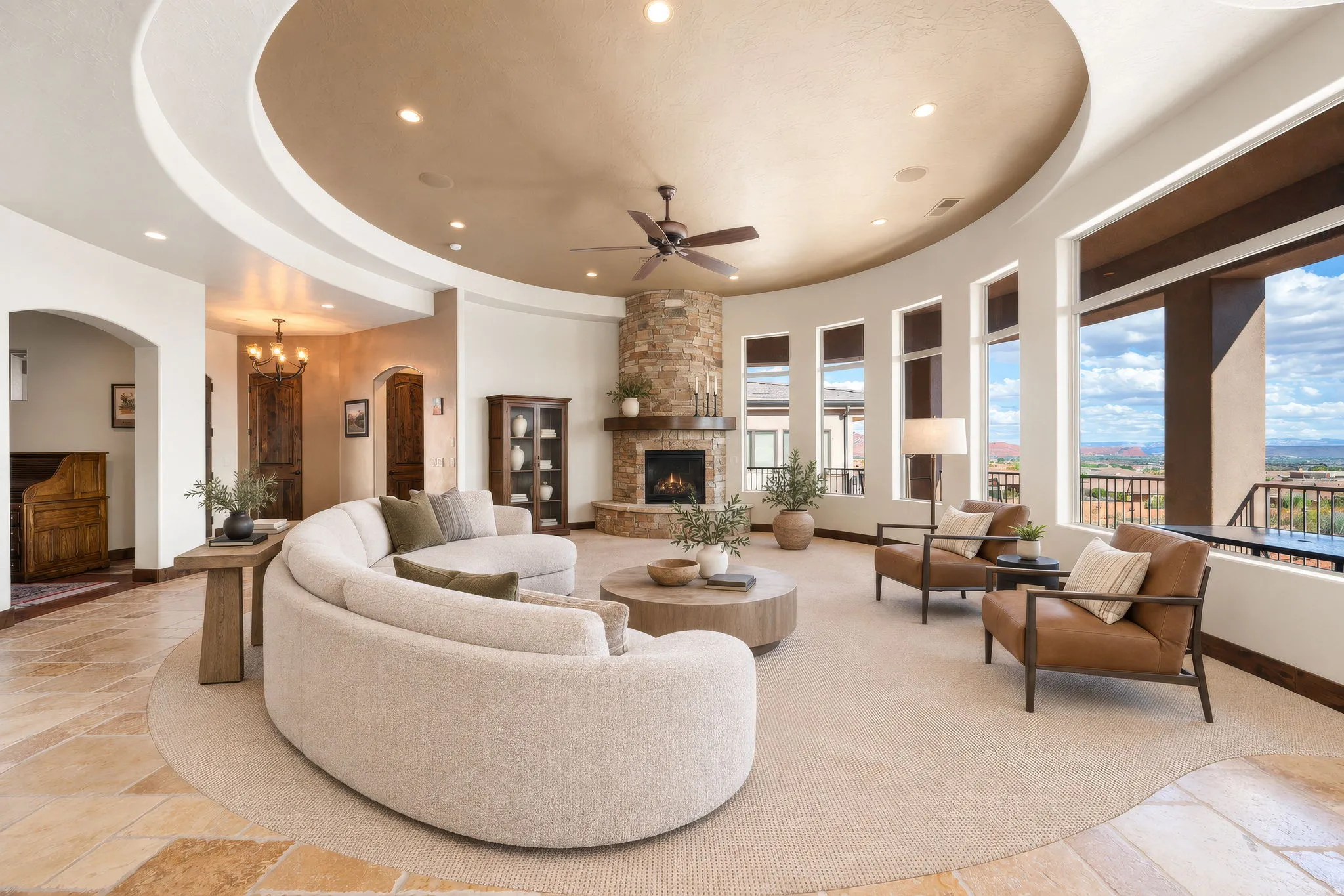 Curved architectural elements with recessed lighting, stone-clad fireplace with mantel, ceiling fan, and multiple floor-to-ceiling windows