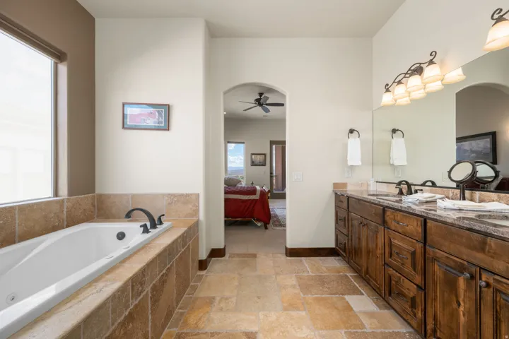 Spacious bathroom featuring a built-in soaking tub, a dual vanity with wood cabinetry, and a large mirror with integrated lighting