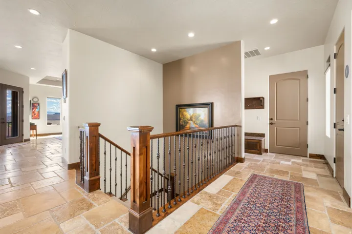 Stone tile flooring, recessed ceiling lighting, wood and wrought iron staircase railing, arched panel door, and built-in entry bench