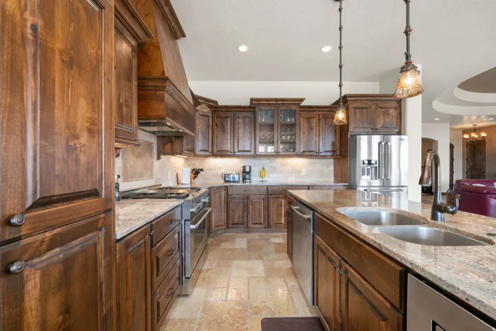Custom wood cabinetry, stainless steel appliances, dual basin island sink, pendant lighting, and tiled flooring