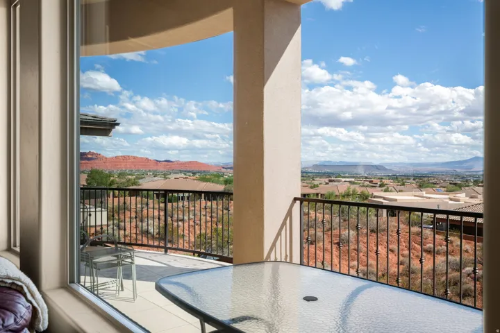 Expansive balcony featuring wrought iron railing, a glass-top outdoor table, and panoramic desert scenery