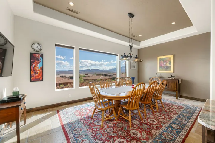 Large windows with distant scenery, tray ceiling with recessed lighting, stone tile flooring, and a decorative pendant light fixture