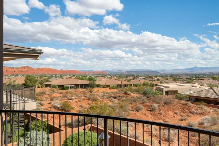 Balcony with wrought iron railing overlooking a desert landscape with distant red rock formations and residential structures