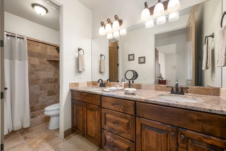 Dual vanity with integrated sinks, granite countertop, rich wood-finish cabinetry, and framed mirror