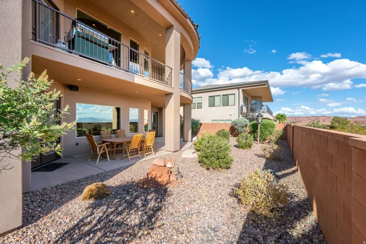 Curved exterior architecture, ground-level patio, upper-level balcony with metal railing, expansive windows, and a landscaped rock garden