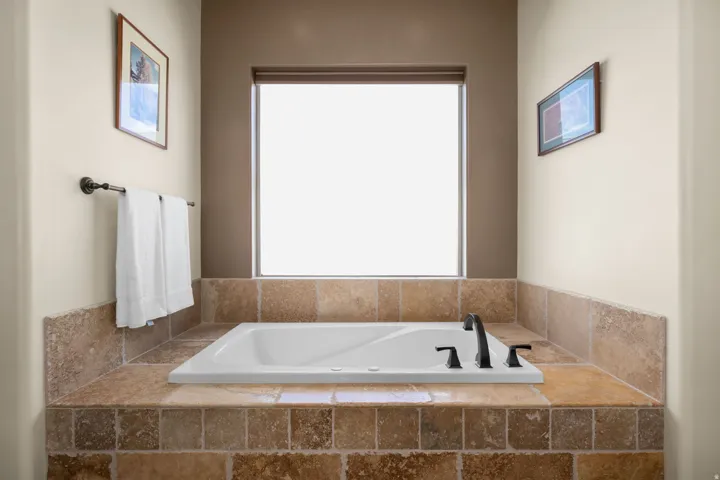 Built-in bathtub surrounded by natural stone tile, featuring a matte black faucet and window